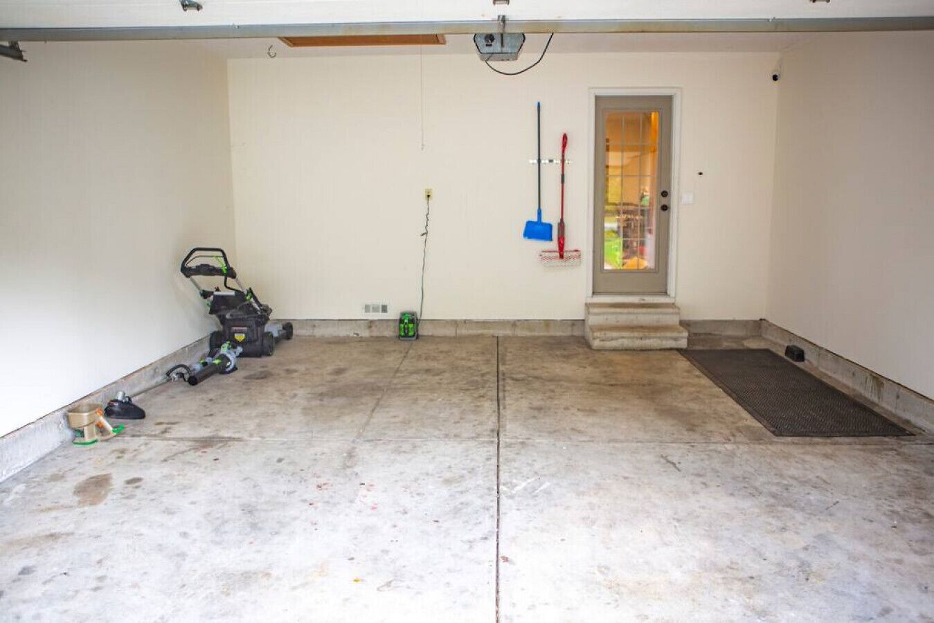Un garaje con piso de concreto, cortacésped y una puerta con ventana.