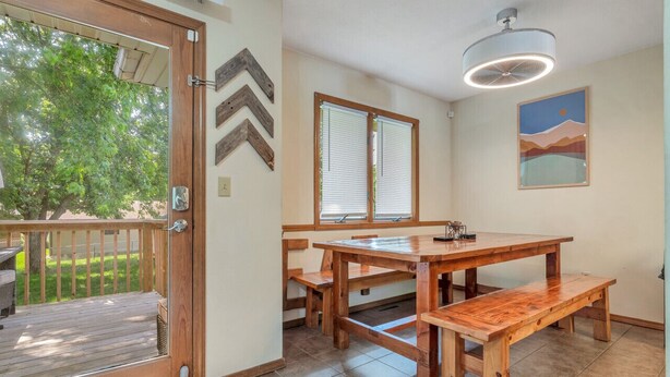 Una mesa de comedor de madera con bancos, un ventilador de techo y vistas al exterior a través de una puerta.