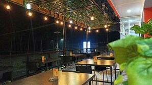 An indoor dining area with tables and chairs, a high ceiling with exposed beams, and string lights. - Mel's Inn Manado (Manado)