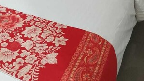 A neatly made bed with white bedding and a red floral throw. - Mel's Inn Manado (Manado)