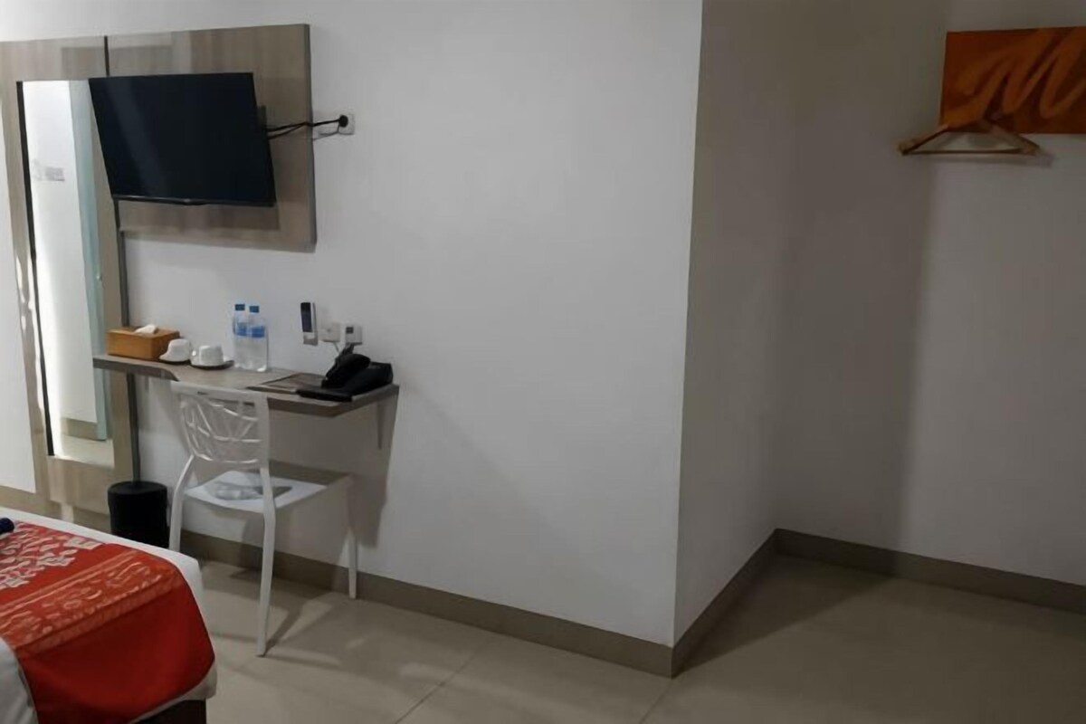 A hotel room with a bed, a desk with a chair, a television, and a small table with a basket and a water bottle.
