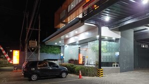 A modern building with a glass facade, a parked car, and a pedestrian walkway. - Mel's Inn Manado (Manado)
