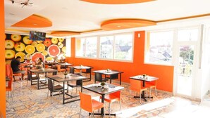 A restaurant with orange walls and a tiled floor, featuring multiple tables and chairs. - Mel's Inn Manado (Manado)