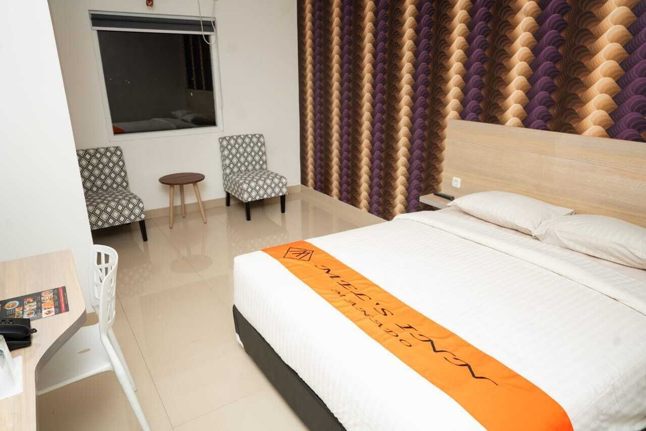 A hotel room with a bed, two patterned chairs, a small table, and a window.