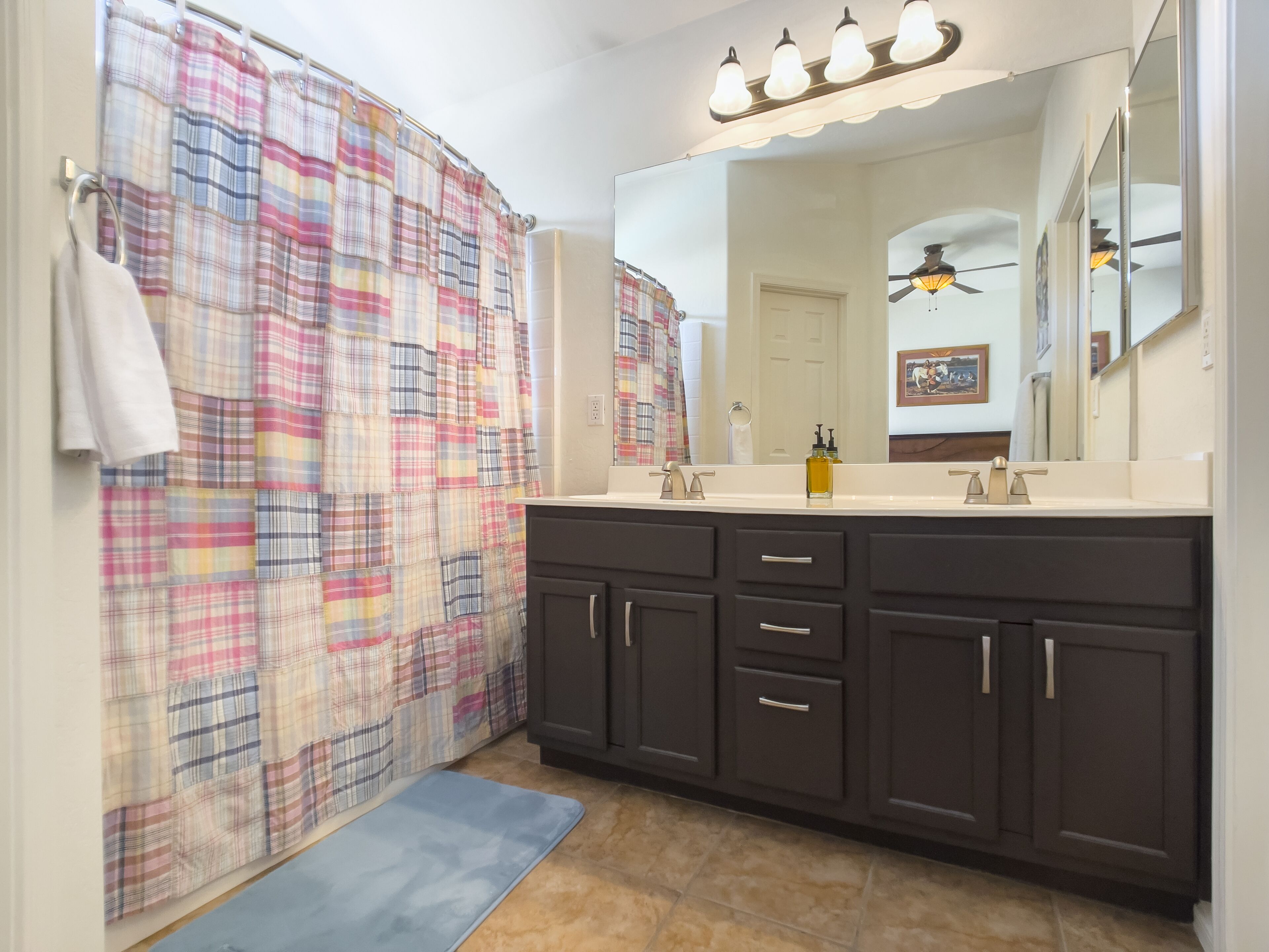 A bathroom with a plaid shower curtain, dark cabinets, a white sink, and a ceiling fan.
