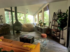 A cozy living room with a fireplace, large windows, a bookshelf, and a variety of plants. - Mid-Century house in the Trees (Smyrna)