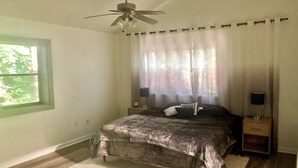 Une chambre à coucher avec un lit, un ventilateur de plafond, une fenêtre et une table de chevet avec une lampe.