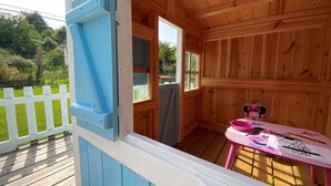 Eine Holzhütte mit blauer Fassade, einem kleinen Tisch mit Kunstbedarf und einer Minnie Maus Figur.