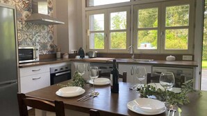 Eine moderne Küche mit Esstisch für vier Personen, einem eingebauten Backofen und einem großen Fenster mit Blick auf Grünflächen.