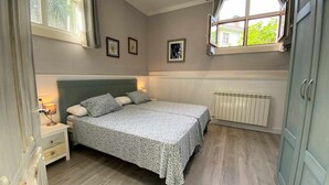 Ein Schlafzimmer mit Bett, Nachttischen, Heizkörper und einem Fenster mit Vorhängen.