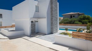 Un edificio moderno de color blanco con un detalle de pared de piedra, piscina y terraza de madera.