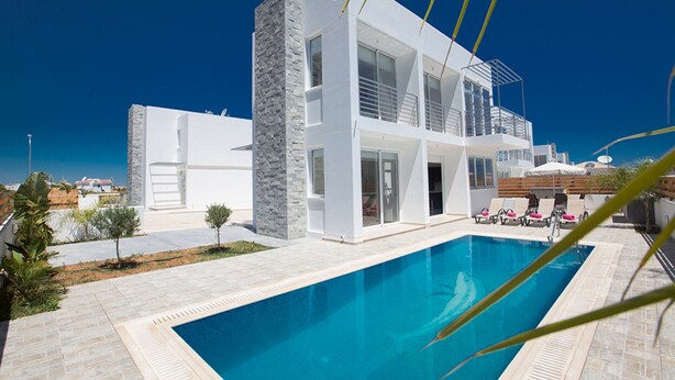 Una casa moderna de dos pisos con piscina, destacando un revestimiento de piedra y un balcón con sillones de descanso.
