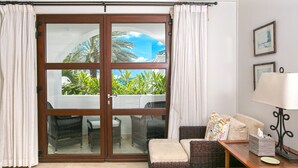 A living room with a sliding glass door leading to a balcony, wicker furniture, a table with a lamp, and framed pictures on the wall. - Blue Dove | Beach Front - Located in  Beautiful Cupecoy with Private Pool (Cupecoy)