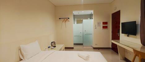 A hotel room with a bed, a desk with a TV, a telephone, and a kettle.