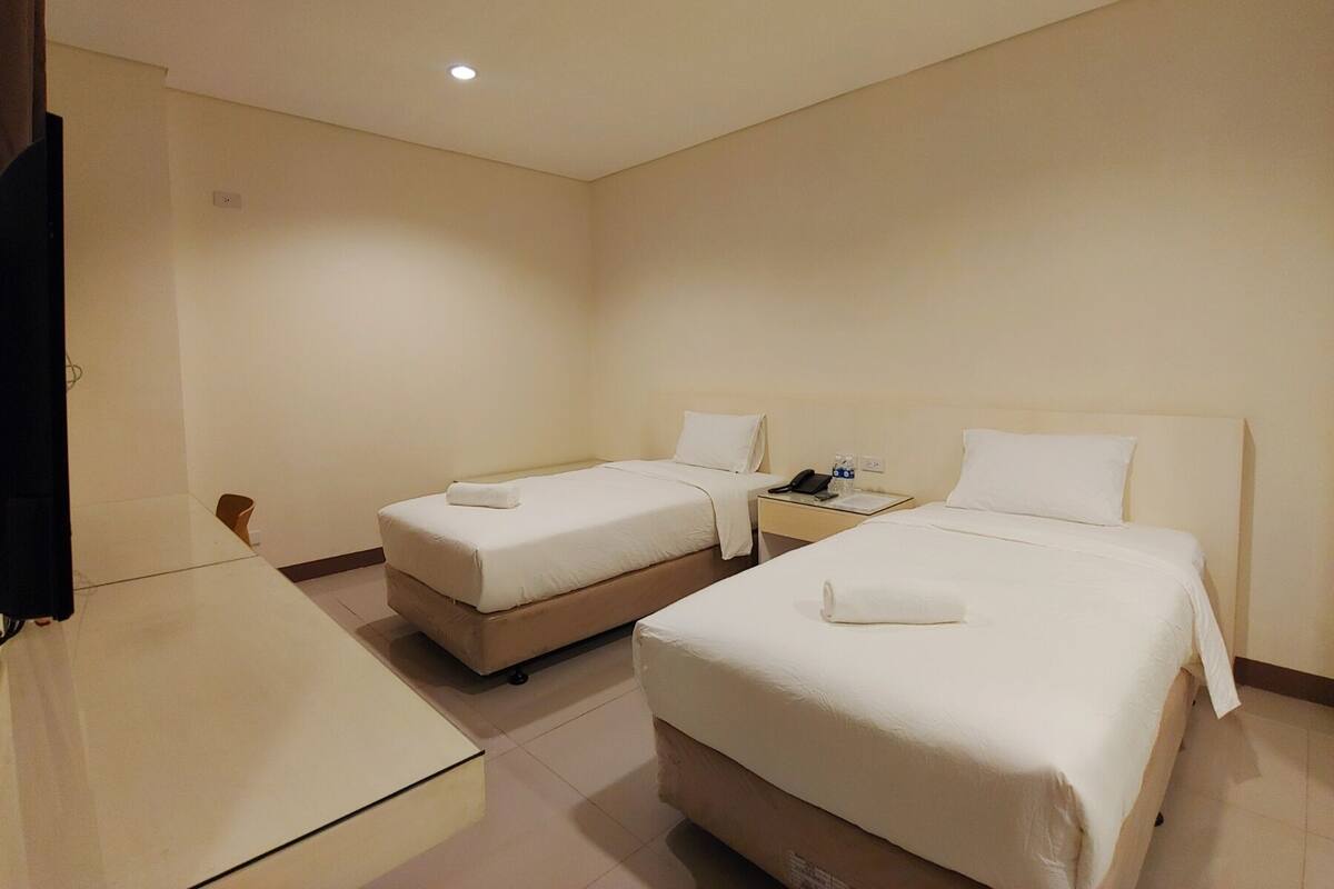 A hotel room with two beds, a desk, and a television.