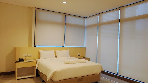 A modern hotel room with a large bed, bedside tables, and a window with blinds. - Kaizen Suites (Manila)