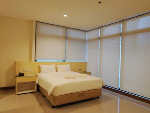 A modern hotel room with a large bed, bedside tables, and a window with blinds. - Kaizen Suites (Manila)