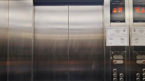 An elevator interior with stainless steel doors, a digital display, emergency call button, and a no-smoking sign. - Kaizen Suites (Manila)