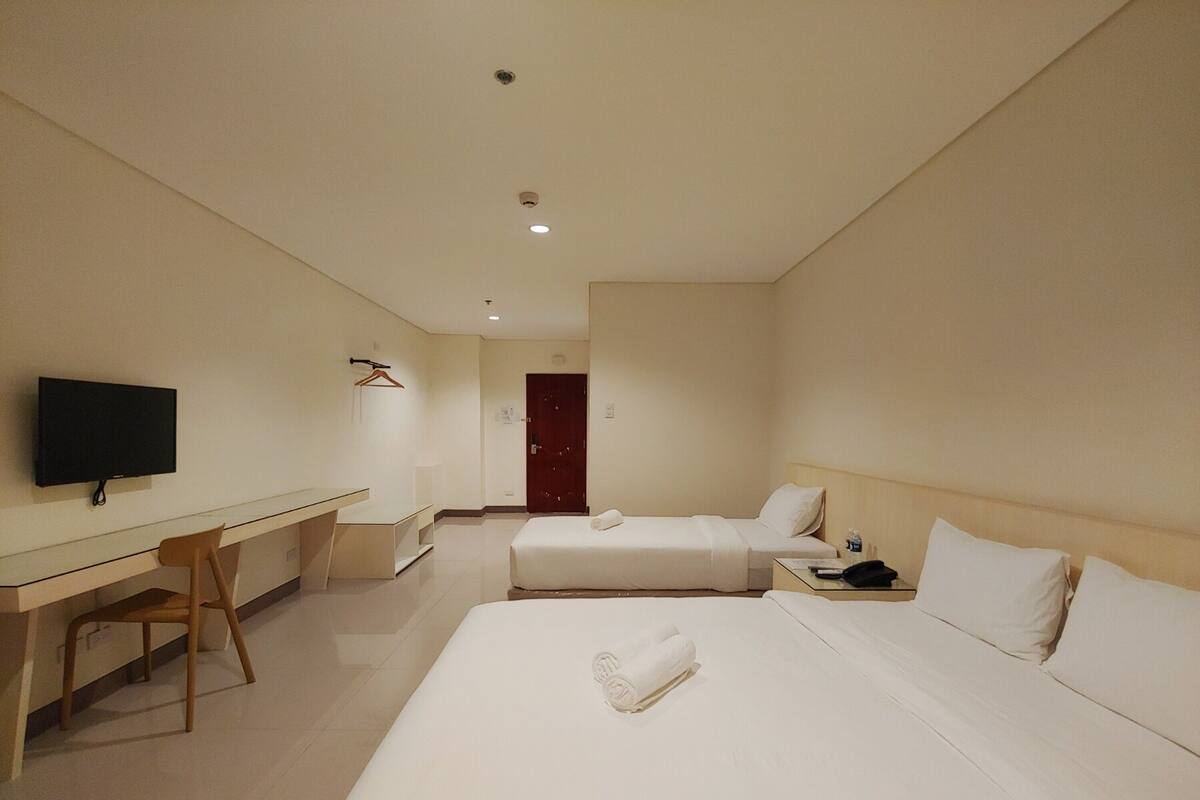 A hotel room with two beds, a desk, a television, and a door.