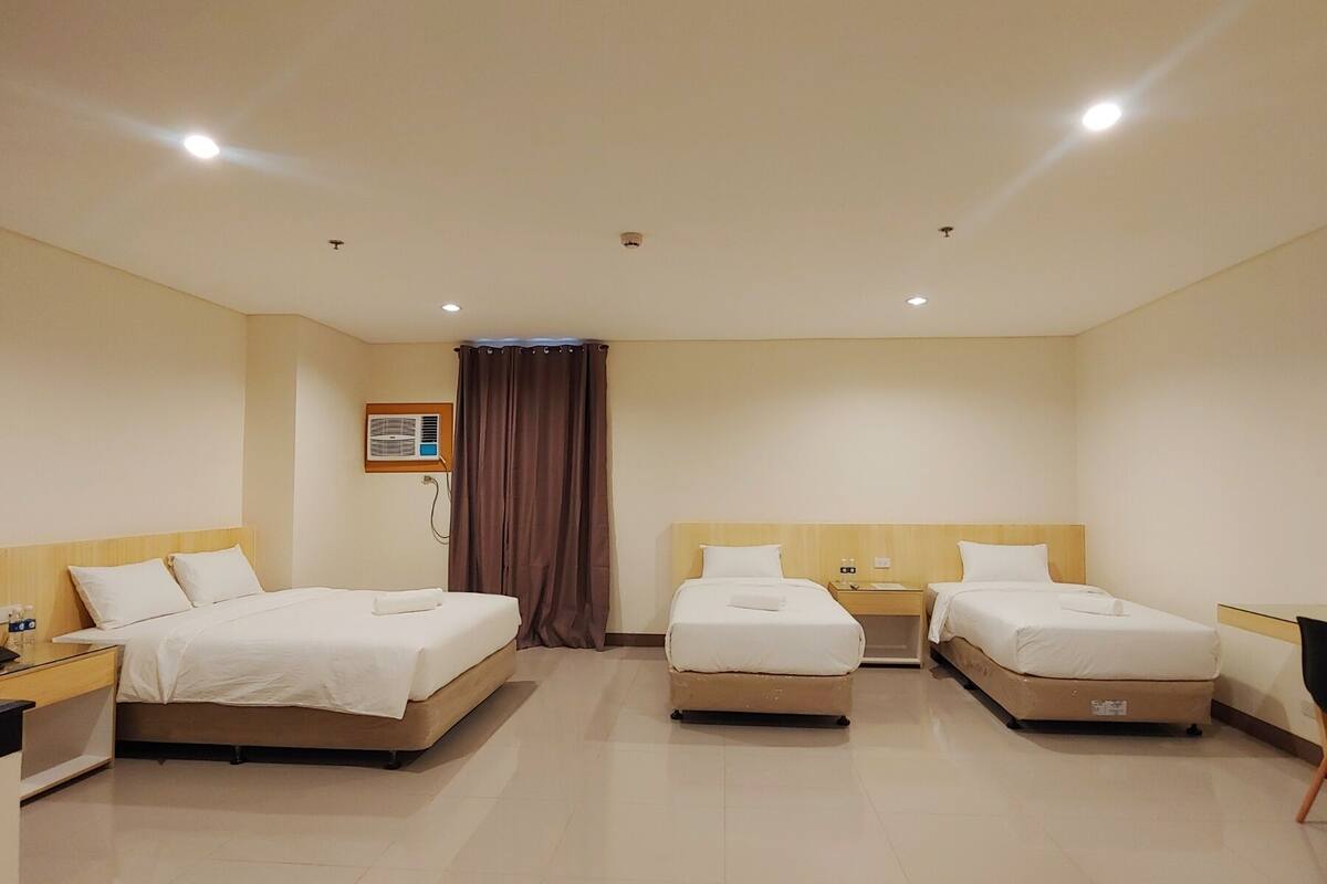 A hotel room with two single beds, a small table, a chair, and a wall-mounted air conditioning unit.