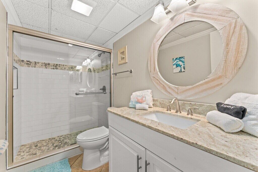A bathroom with a glass-enclosed shower, a sink with a mirror, and a toilet.