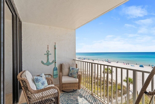 A balcony with wicker furniture, a view of the beach, and a decorative anchor.