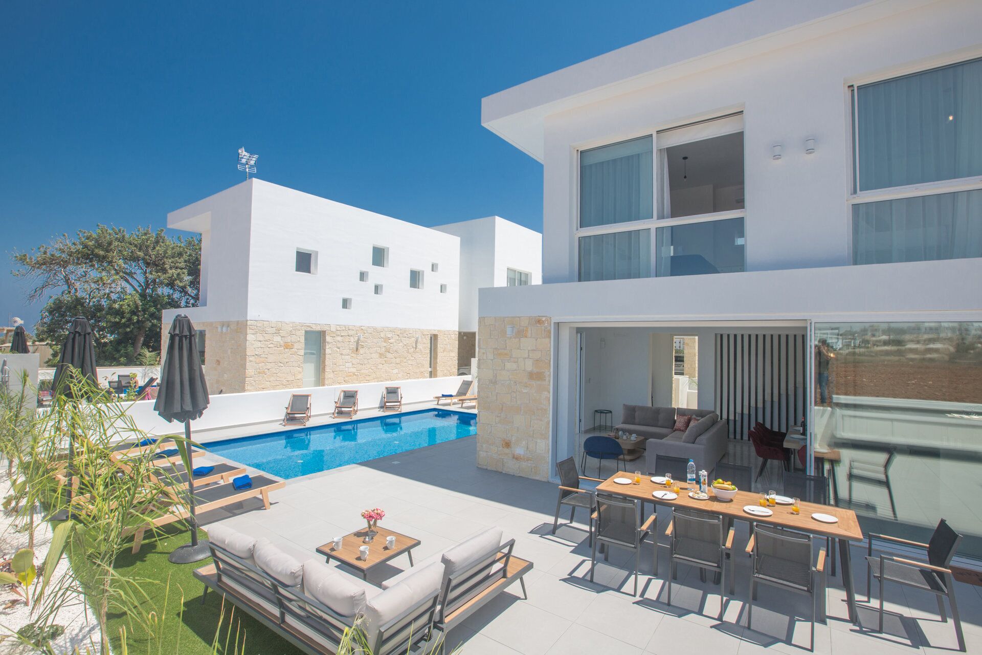 Una casa moderna de dos pisos con piscina, mobiliario exterior y comedor.