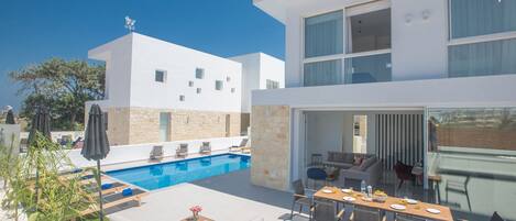 Una casa moderna de dos pisos con piscina, mobiliario exterior y comedor.