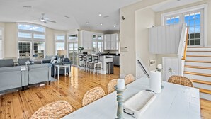 A spacious living area with a grey sofa, wooden flooring, and a kitchen in the background.