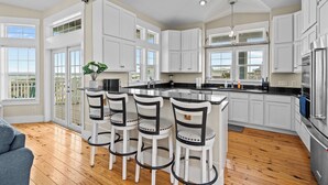 A modern kitchen with white cabinets, a central island with bar stools, and a large window providing natural light.
