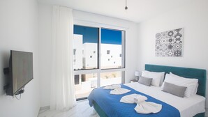Een moderne hotelkamer met een groot bed, wit- en blauwe beddengoed, een flatscreen televisie en uitzicht op gebouwen.