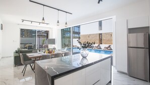 Een moderne keuken met een marmeren aanrecht, een eethoek met een tafel en stoelen, een groot raam en uitzicht op een buitenzwembad.