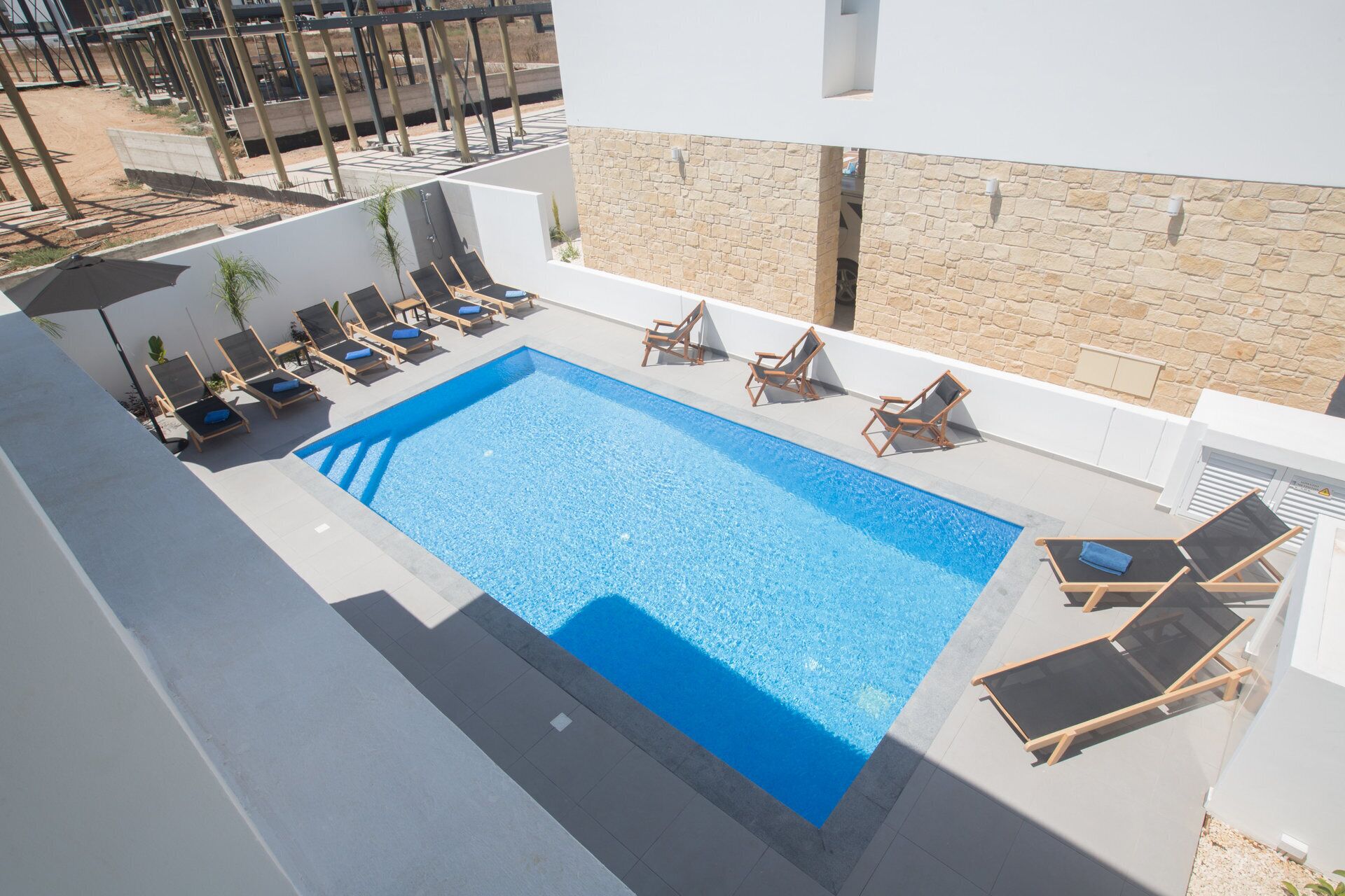 A rooftop pool with multiple sun loungers and a stone wall.