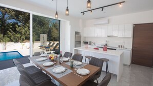 Un espace repas moderne avec vue sur la piscine, une cuisine dotée de meubles blancs et un coin bar.