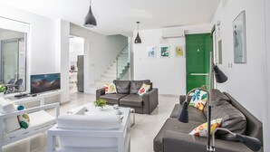 Un salon moderne avec un canapé, une table basse et un téléviseur. Un escalier mène à un autre niveau.