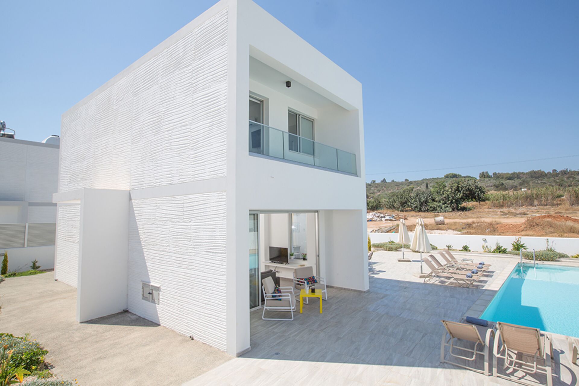 Ein modernes, zweistöckiges Haus mit einem großen Balkon, einem Pool und Sitzgelegenheiten im Freien.