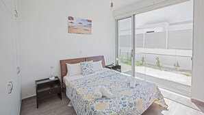 A bedroom with a bed, a nightstand, a lamp, a painting, and a sliding glass door to a balcony. - The Complete Guide to Renting Your Exclusive Holiday Villa in Protaras with Private Pool and Close to the Beach (Protaras)