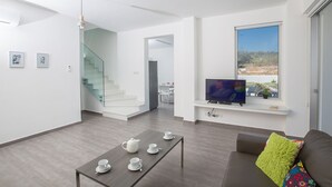 A modern living room with a flat-screen TV, a sofa with a colorful pillow, a dining area with a table set for tea, and a staircase leading to another room. - The Complete Guide to Renting Your Exclusive Holiday Villa in Protaras with Private Pool and Close to the Beach (Protaras)