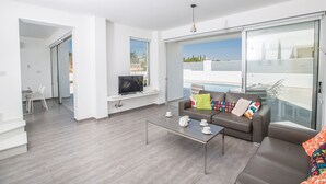 A modern living room with a sofa, coffee table, and TV. There is a sliding glass door leading to a balcony with a pool view. - The Complete Guide to Renting Your Exclusive Holiday Villa in Protaras with Private Pool and Close to the Beach (Protaras)