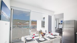 A modern kitchen with a stainless steel refrigerator, a dining area with a table set for two, and a view of a pool and outdoor seating area. - Protaras Holiday Villa with Private Pool, Protaras Villa 1554 (Protaras)