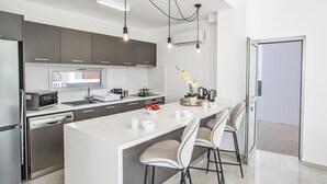 Une cuisine moderne dotée d’un îlot central, d’appareils électroménagers en acier inoxydable et de luminaires suspendus.