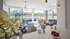 Un salon moderne avec vue sur la piscine, doté de meubles blancs et de luminaires suspendus.