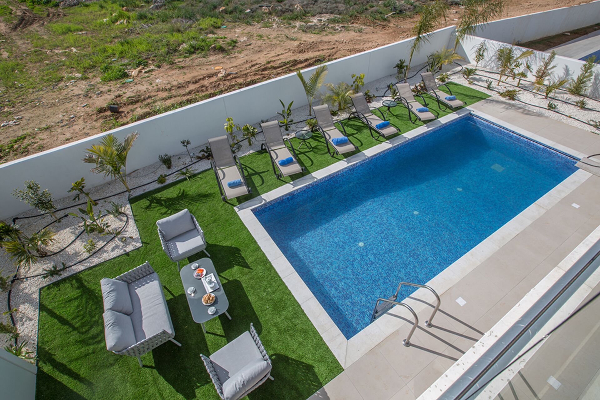 A rooftop pool with a clear blue pool, surrounded by lounge chairs and a small table with a drink.