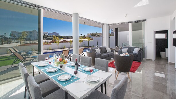 A modern dining area with a view of the city, a pool, and a living area with sofas and a red rug.