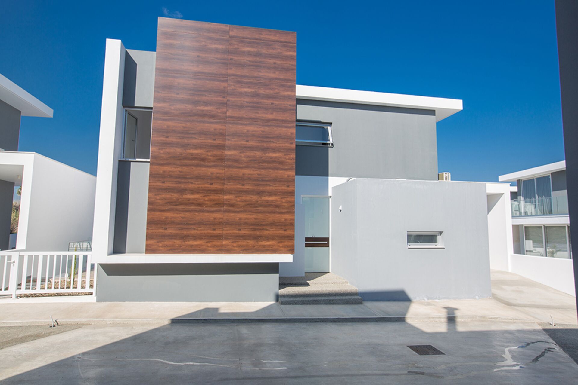 Un edificio moderno con un gran panel de madera, fachada blanca y cielo azul despejado.