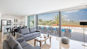 A modern living room with a grey sofa, a coffee table, and a view of a swimming pool and landscape.