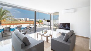 A modern living room with a pool, large windows, and a flat-screen TV.
