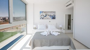 Ett modernt hotellrum med en stor säng, en tavla ovanför sängen och utsikt över staden genom ett stort fönster.