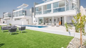 Ett modernt hus i två våningar med en swimmingpool, en uteplats och en välskött gräsmatta.