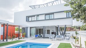 A modern two-story house with a swimming pool, outdoor seating area, and a glass door entrance. - Your Dream Holiday Villa with Private Pool in Protaras most Exclusive Neighbourhood (Protaras)